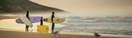 Family standing on the shore with surf boards looking out at waves